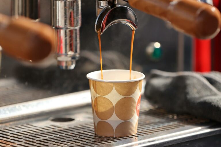 Close-up of espresso flowing into a paper cup from a coffee machine in a cafe setting.