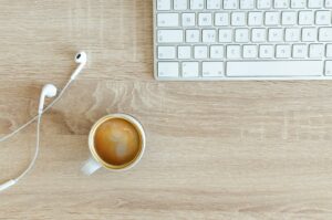 beverage filled mug near apple airpods with lightning connector and apple magic keyboard