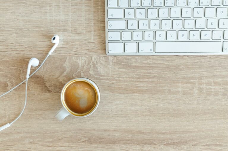 beverage filled mug near apple airpods with lightning connector and apple magic keyboard